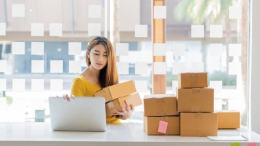  Small Business Startup Freelance SME Entrepreneurs Beautiful Asian Young Women Working at Home with Box, Smartphone, Laptop on the Table with Online Sales, Marketing, Packaging, SME Shipping, Ecommerc