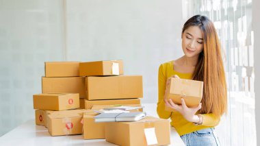 Small Business Startup Freelance SME Entrepreneurs Beautiful Asian Young Women Working at Home with Box, Smartphone, Laptop on the Table with Online Sales, Marketing, Packaging, SME Shipping, Ecommerc