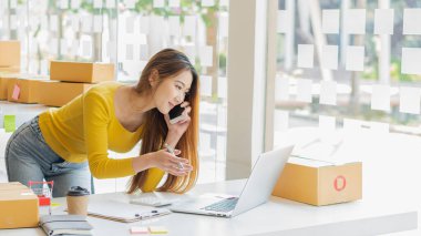 Small Business Startup Freelance SME Entrepreneurs Beautiful Asian Young Women Working at Home with Box, Smartphone, Laptop on the Table with Online Sales, Marketing, Packaging, SME Shipping, Ecommerc