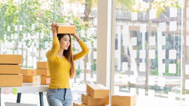 Small Business Startup Freelance SME Entrepreneurs Beautiful Asian Young Women Working at Home with Box, Smartphone, Laptop on the Table with Online Sales, Marketing, Packaging, SME Shipping, Ecommerc