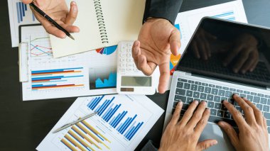 İki işadamı, finans şirketlerinin grafikleri ve analizleri ve hesap makinesi ofislerinin masada kağıtları, laptopları ve kahve fincanları ile kullanımı hakkında konuştular..