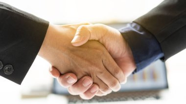  Toplantı bittikten sonra iki işadamı, toplantı odasındaki dizüstü bilgisayarlarla masalarının üzerindeki maliyet grafiklerini analiz ederek el sıkıştı..