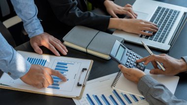Ekonomi ve pazarlama belgeleri, toplantılar, veri analizleri, finansal grafikler ve dizüstü bilgisayarlar ve hesap makineleri ile ofis içi grafikler hakkındaki tartışmalar sırasında iş stratejisini tartışan iş adamları işbirliği yaparlar..