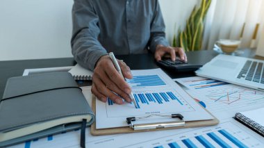 Ekonomi ve pazarlama belgeleri, toplantılar, veri analizleri, finansal grafikler ve dizüstü bilgisayarlar ve hesap makineleri ile ofis içi grafikler hakkındaki tartışmalar sırasında iş stratejisini tartışan iş adamları işbirliği yaparlar..