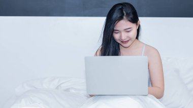 Beyaz bir yatakta dizüstü bilgisayarla çalışan genç bir kadın.