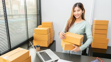 Küçük bir işletme, KOBİ, sahibi, dizüstü bilgisayar kullanan genç Asyalı girişimciler, kutu hazırlamak için İnternet üzerinden siparişleri kontrol ediyorlar. Fikirleri internette sat