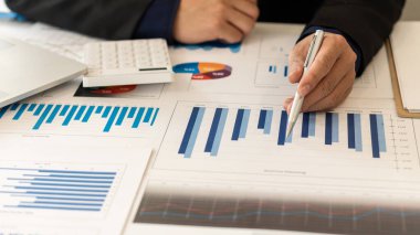 Grafik analiz masasında bir işadamı oturuyor. Ofis hesap makineleriyle grafikler ve çizelgeler üzerinde