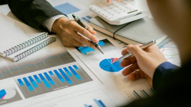 Grafik analiz masasında bir işadamı oturuyor. Ofis hesap makineleriyle grafikler ve çizelgeler üzerinde