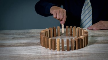 Gri bir arkaplanı ayıran bir masanın üzerindeki binalardan ahşap tuğlaları alan bir adamın kısmi görüntüsü.