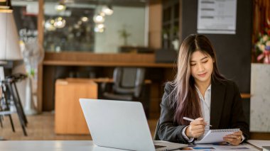 İş yerinde çalışan bir iş kadını istatistiksel analiz masasında elinde dizüstü bilgisayar kullanarak bir çizelge tutuyor.