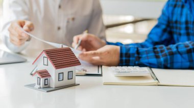 Emlakçılar ev tarzını müşterilere tanıtırken modern ahşap masalarda panolarla kontrat imzalıyorlar. Ev satışları ve kiralama için broker fikirleri.