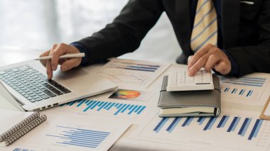 Bilgisayarda, bilgisayarda, bütçede ve grafik kağıdında hesap makinesi kullanan bir iş adamı..