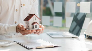 Satılık emlak komisyonculuğu sözleşmeleri ve ofisteki masada bir ev..