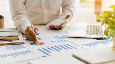 İşadamı, ofisteki gelir tablolarını ve grafikleri dizüstü bilgisayarları ve modern hesap makineleriyle analiz ediyor. Stratejik fikirler.