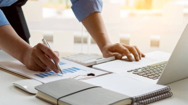 İşadamı, ofisteki gelir tablolarını ve grafikleri dizüstü bilgisayarları ve modern hesap makineleriyle analiz ediyor. Stratejik fikirler.