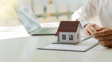 Emlakçılar masalarında dizüstü bilgisayarla ev formları ve sözleşme belgeleri sunuyorlar..
