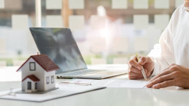 Emlakçılar masalarında dizüstü bilgisayarla ev formları ve sözleşme belgeleri sunuyorlar..