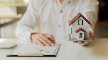 Emlakçılar masalarında dizüstü bilgisayarla ev formları ve sözleşme belgeleri sunuyorlar..