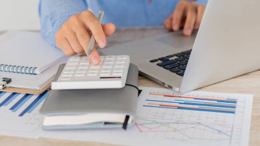 Hesaplamalarla notlar yazmak için bir hesap makinesi kullanan yakın plan iş adamları, mali muhasebe kavramları üzerinde grafik analizi.