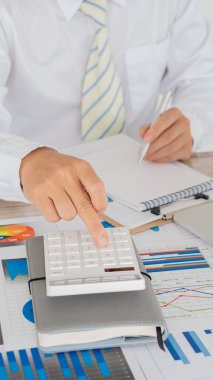 Hesaplamalarla notlar yazmak için bir hesap makinesi kullanan yakın plan iş adamları, mali muhasebe kavramları üzerinde grafik analizi.