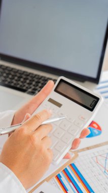 Hesaplamalarla notlar yazmak için bir hesap makinesi kullanan yakın plan iş adamları, mali muhasebe kavramları üzerinde grafik analizi.