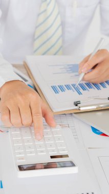 Hesaplamalarla notlar yazmak için bir hesap makinesi kullanan yakın plan iş adamları, mali muhasebe kavramları üzerinde grafik analizi.
