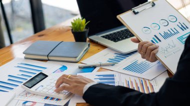 Hesaplamalarla notlar yazmak için bir hesap makinesi kullanan yakın plan iş adamları, mali muhasebe kavramları üzerinde grafik analizi.