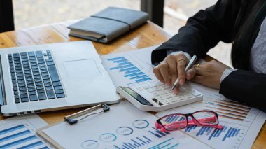 Hesaplamalarla notlar yazmak için bir hesap makinesi kullanan yakın plan iş adamları, mali muhasebe kavramları üzerinde grafik analizi.