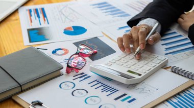 Hesaplamalarla notlar yazmak için bir hesap makinesi kullanan yakın plan iş adamları, mali muhasebe kavramları üzerinde grafik analizi.