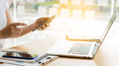 Bir kafede oturan genç bir kadın dizüstü bilgisayarlı bir masada akıllı telefon kullanıyor. Genç kadınlar internette sohbet blogunda sörf yapıyor.