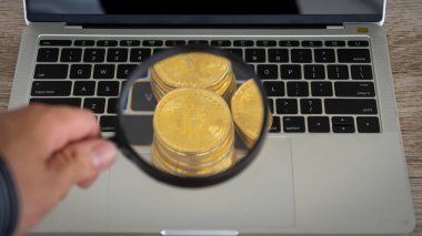Dizüstü bilgisayarda Bitcoin sikkeler ve büyüteç tutan bir el kukla pazarına bakıyor..