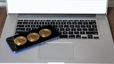 Bir telefon ve dizüstü bilgisayara yerleştirilmiş Bitcoin para. Borsa konsepti.