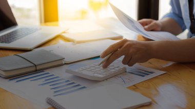 Genç işadamı, şirketin mali belgelerinin numaralarını hesaplamak için sayısal bir hesap makinesi kullanıyor. Şirketin finansal grafiklerini analiz ediyor..