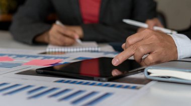 Bir iş adamı tablet bilgisayarla çalışıyor ve ofisteki finans grafiklerini analiz ediyor.