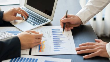 İş analistleri masalarında dizüstü bilgisayarlarla yatırım maliyetleri, emlak ve diğer vergi sistemlerinin grafiklerini oluşturuyorlar.