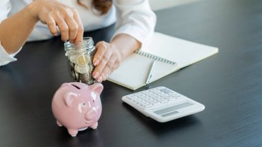 Muhasebe, planlama ve tasarruf fikirleriyle kumbaraya bozuk para koyan genç bir kadın..