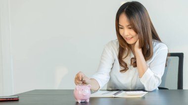 Muhasebe, planlama ve tasarruf fikirleriyle kumbaraya bozuk para koyan genç bir kadın..