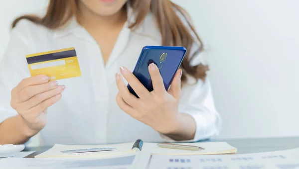 Credit card in hand with phone and laptop to shop online.