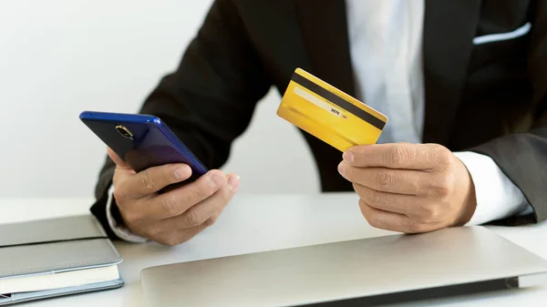 Credit card in hand with phone and laptop to shop online.