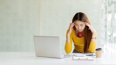 Bilgisayarda çalışan Asyalı kadın, iş sırasında başı ağrıyan kahvecide kahve içiyor.