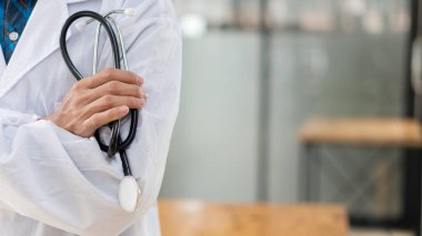 Doktor steteskop tutuyor ve kolları kapalı bulanık bir zeminde duruyor. Asya modeli.