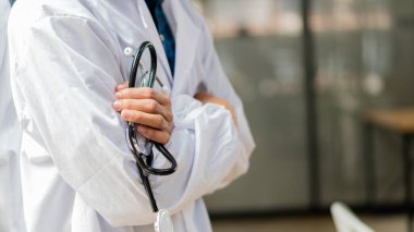 Doktor steteskop tutuyor ve kolları kapalı bulanık bir zeminde duruyor. Asya modeli.