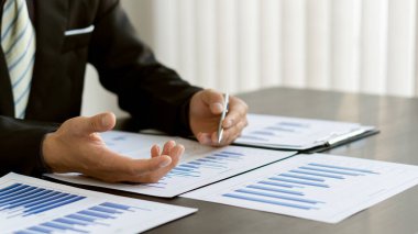 Genç bir finans analisti, ahşap bir masada otururken dizüstü bilgisayarında çalışıyor. Şirketin tasarımlarını inceleyen ve hesaplayan bir işadamı.