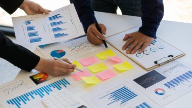 Şirketin çoklu analiz ve hesaplamalarında dizüstü bilgisayar ve grafik belgeleriyle çalışan genç işadamı.