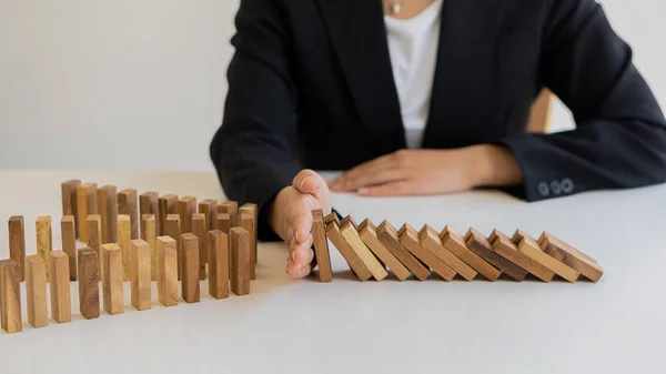 risk control concept A businessman defends a falling wooden block and a construction business risk strategy to select and protect the wooden blocks that line up on the table.