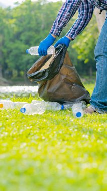 Genç adam, çevreyi korumak için parkta temizlik yapmak için çöp torbalarında plastik şişeler topluyor..