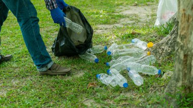 Genç adam, çevreyi korumak için parkta temizlik yapmak için çöp torbalarında plastik şişeler topluyor..