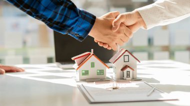 Emlakçılar, ofiste belgelenmiş bir ev almak için müstakbel müşterilerle tokalaşıyor. Ve müşterilere sigortalı satın almaları için bir ev modeli sunacağız.