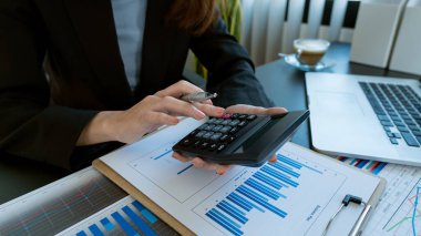 İş adamı elinde kalem tutuyor ve hesap makinesine basıyor. Hesaplamak ve analiz etmek için ve masada dizüstü bilgisayarla ofiste.