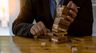 İş adamı masaya tahta kule blokları koyuyor, risk kontrol konsepti. İnşaat ve savunma sektöründe planlama ve strateji